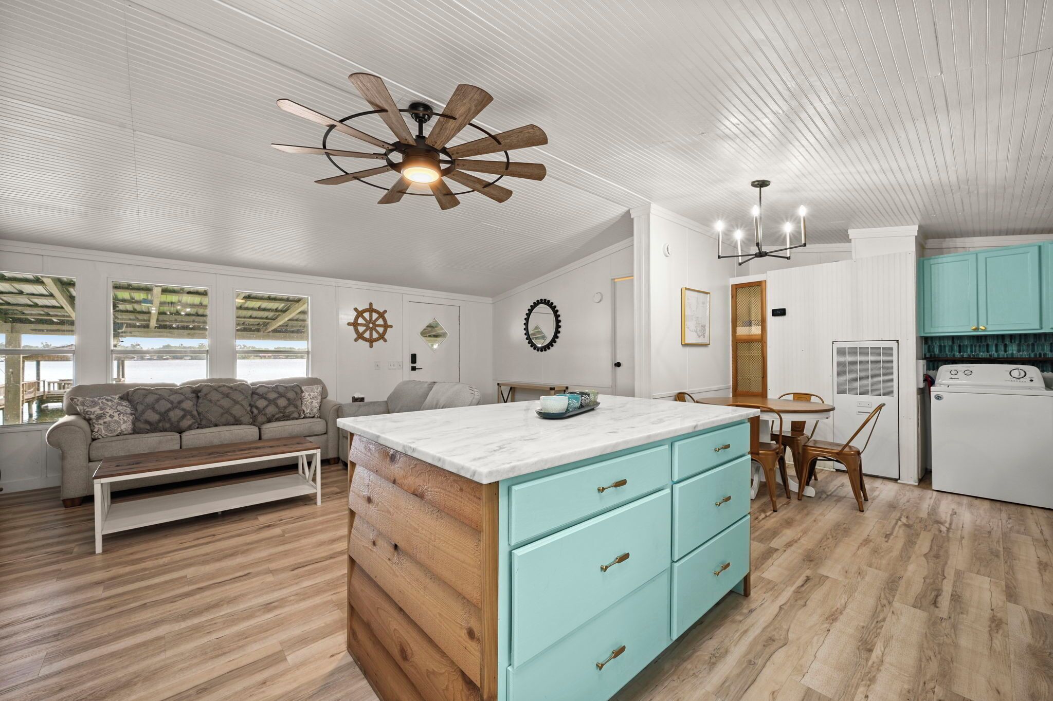 A spacious living area with a wooden coffee table, a sofa, and a kitchen with light blue cabinets and a white washing machine.