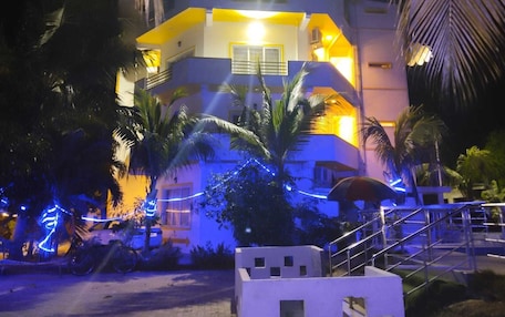 A multi-story building with balconies, surrounded by palm trees and illuminated by warm lighting.