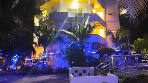 Un immeuble à plusieurs étages doté de balcons, entouré de palmiers et illuminé par un éclairage chaleureux.