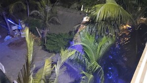 Une vue nocturne d’un complexe hôtelier tropical, avec des palmiers et un petit espace piscine.
