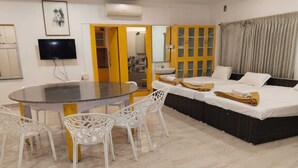Une chambre d’hôtel moderne dotée d’un grand lit, d’une table à manger avec des chaises, d’une télévision et d’une salle de bain avec un miroir et un lavabo.