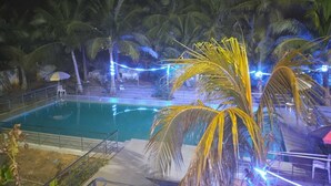 Un espace piscine aménagé pour la nuit, avec des palmiers et des guirlandes lumineuses.