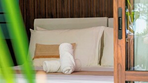 A bed with white bedding and a brown pillow, a rolled towel, and a wooden panel wall.