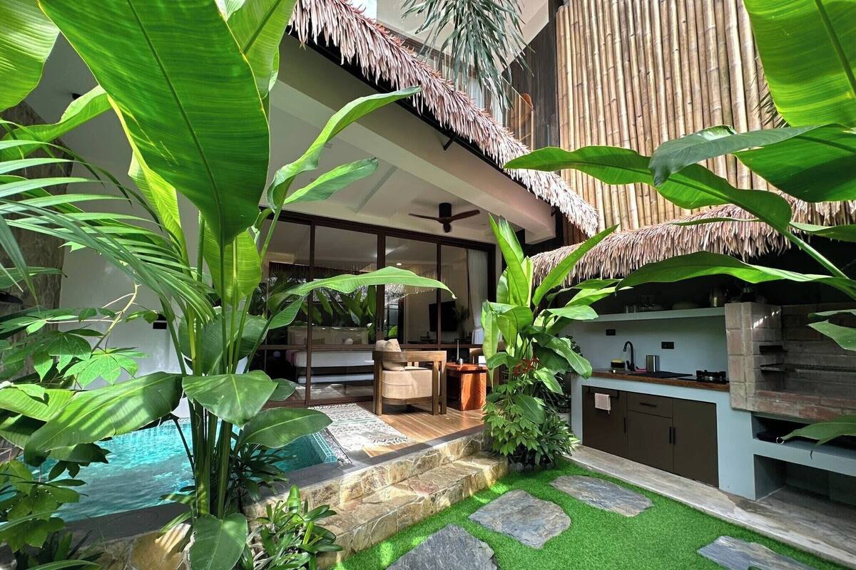 Un espacio exterior moderno con piscina, escalones de piedra y plantas tropicales.