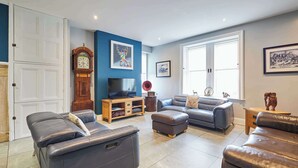 A living room with a grey sofa, a wooden coffee table, a television, and a large window. - Mount Cottage, 5-beds, Sleeps 10, Pet Friendly (Newcastle-upon-Tyne)