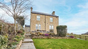 A two-story stone house with a stone pathway leading to the front door, surrounded by a well-maintained garden with various plants and a small lawn. - Mount Cottage, 5-beds, Sleeps 10, Pet Friendly (Newcastle-upon-Tyne)