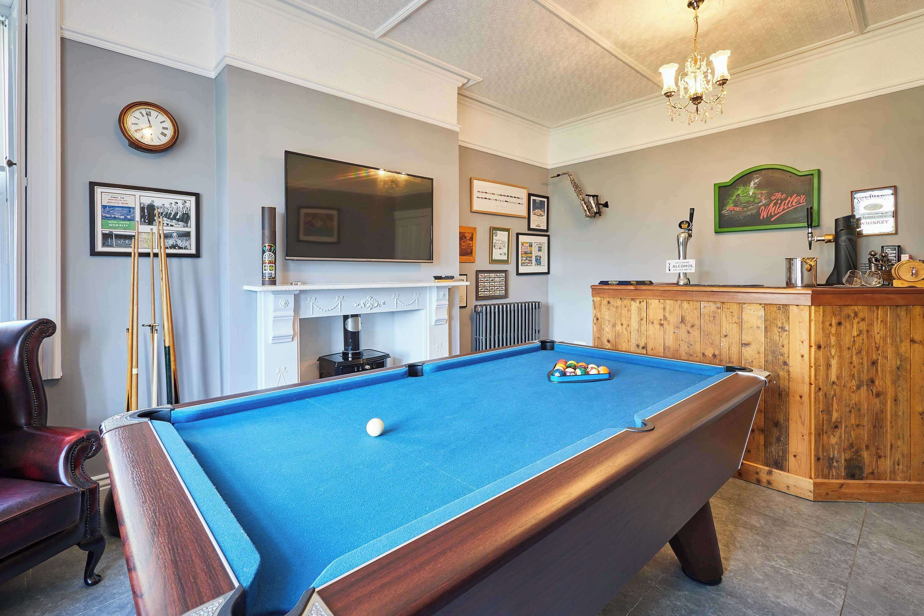 A pool table with a billiard ball, a television mounted on the wall, and a bar area with a sign indicating alcohol service.