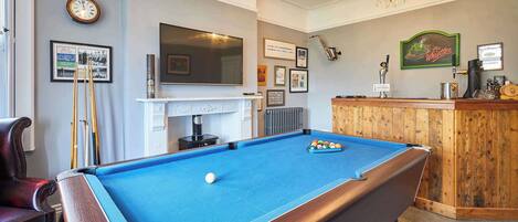 A pool table with a billiard ball, a television mounted on the wall, and a bar area with a sign indicating alcohol service.