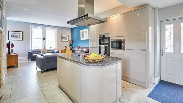 A modern kitchen with a central island, built-in appliances, and a cozy living area with a sofa and a dining table. - Mount Cottage, 5-beds, Sleeps 10, Pet Friendly (Newcastle-upon-Tyne)