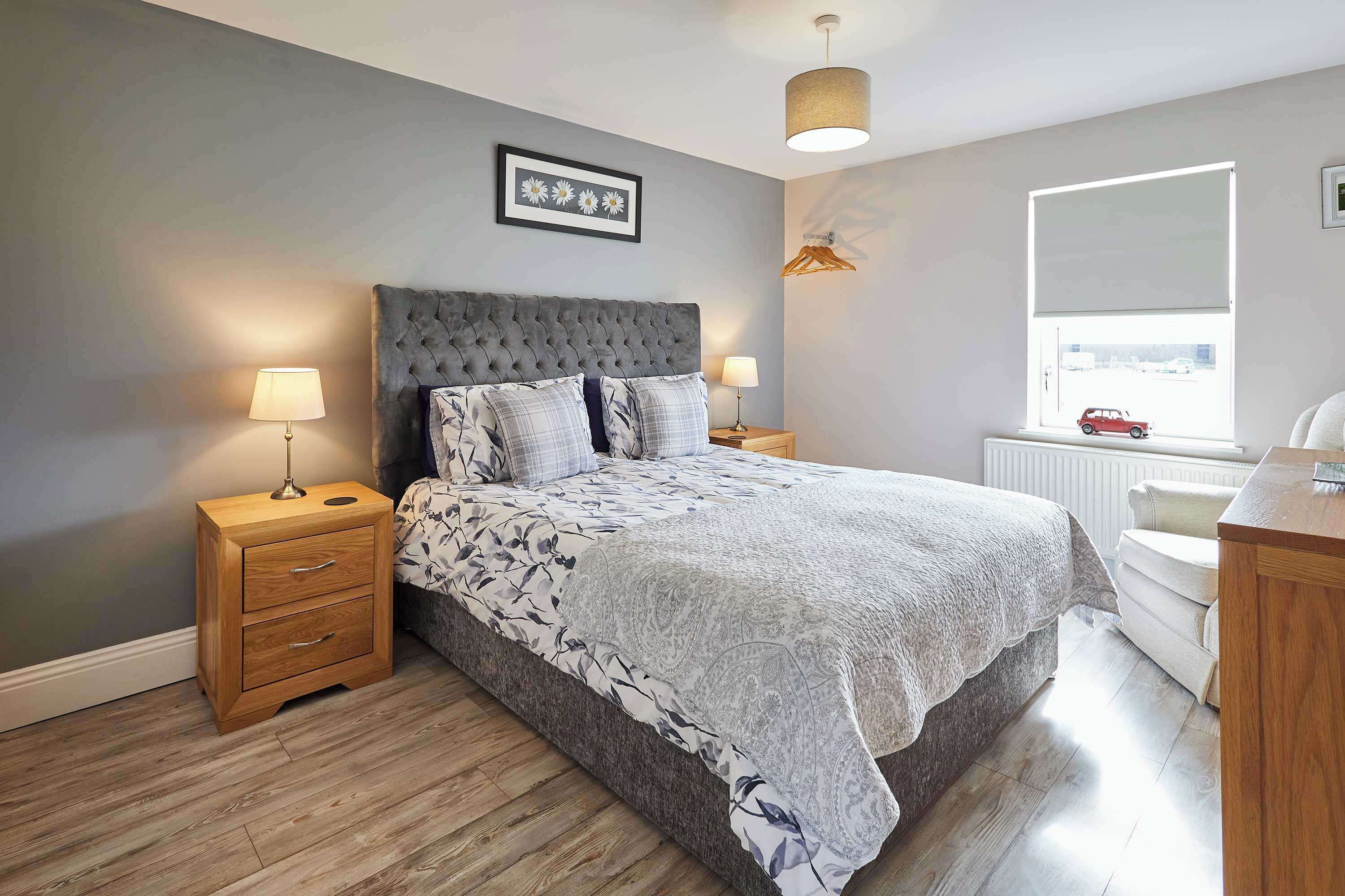 A bedroom with a large bed, two bedside tables with lamps, a window with a view, and a radiator.