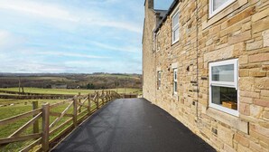 A stone building with a paved walkway and a wooden fence overlooking a rural landscape. - Mount Cottage, 5-beds, Sleeps 10, Pet Friendly (Newcastle-upon-Tyne)