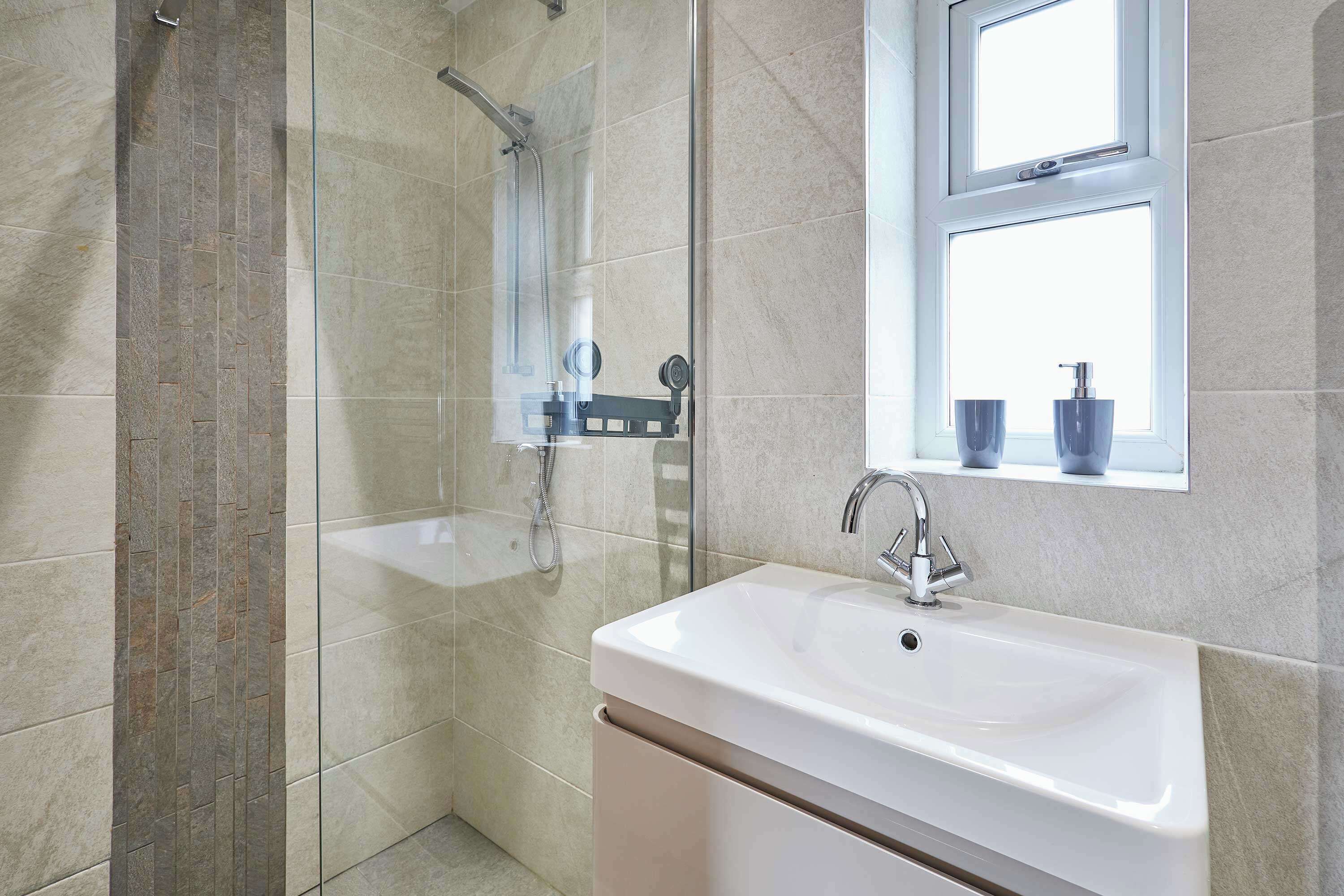 Un baño moderno con cabina de ducha de vidrio, un lavamanos blanco y un ventanal sobre el lavabo.