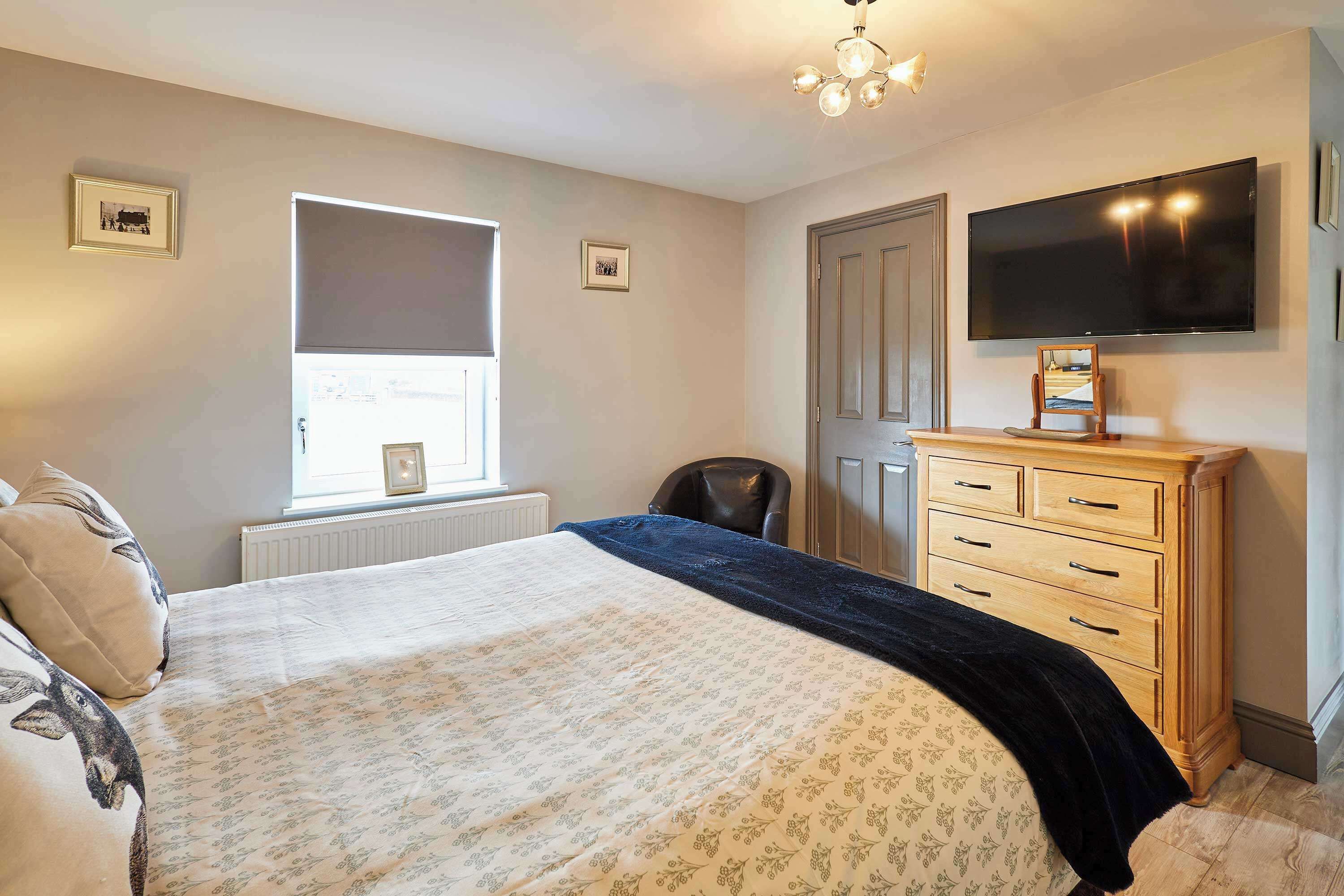 A bedroom with a bed, a dresser, a chair, a TV, and a window.