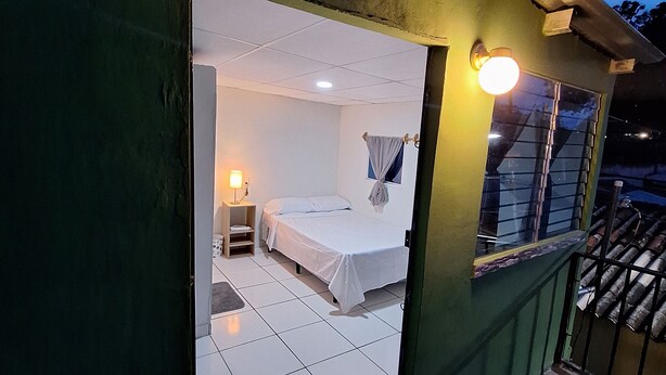 A small, enclosed room with a bed, a nightstand, and a window. - Single Room  (Santa Ana)