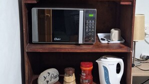 A kitchenette with a refrigerator, microwave, kettle, and a shelf with a stone, jar, and a mug. - Single Room  (Santa Ana)