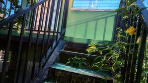 A staircase with a metal railing leading to a building with a green exterior and a window with horizontal bars. - Single Room  (Santa Ana)