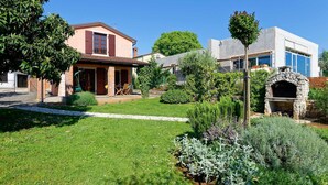 Une propriété résidentielle dotée d’un jardin bien entretenu, d’un four extérieur en pierre et d’une maison à deux étages avec un balcon.