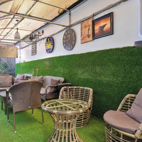 An outdoor seating area with wicker furniture, a green wall, and a clock.