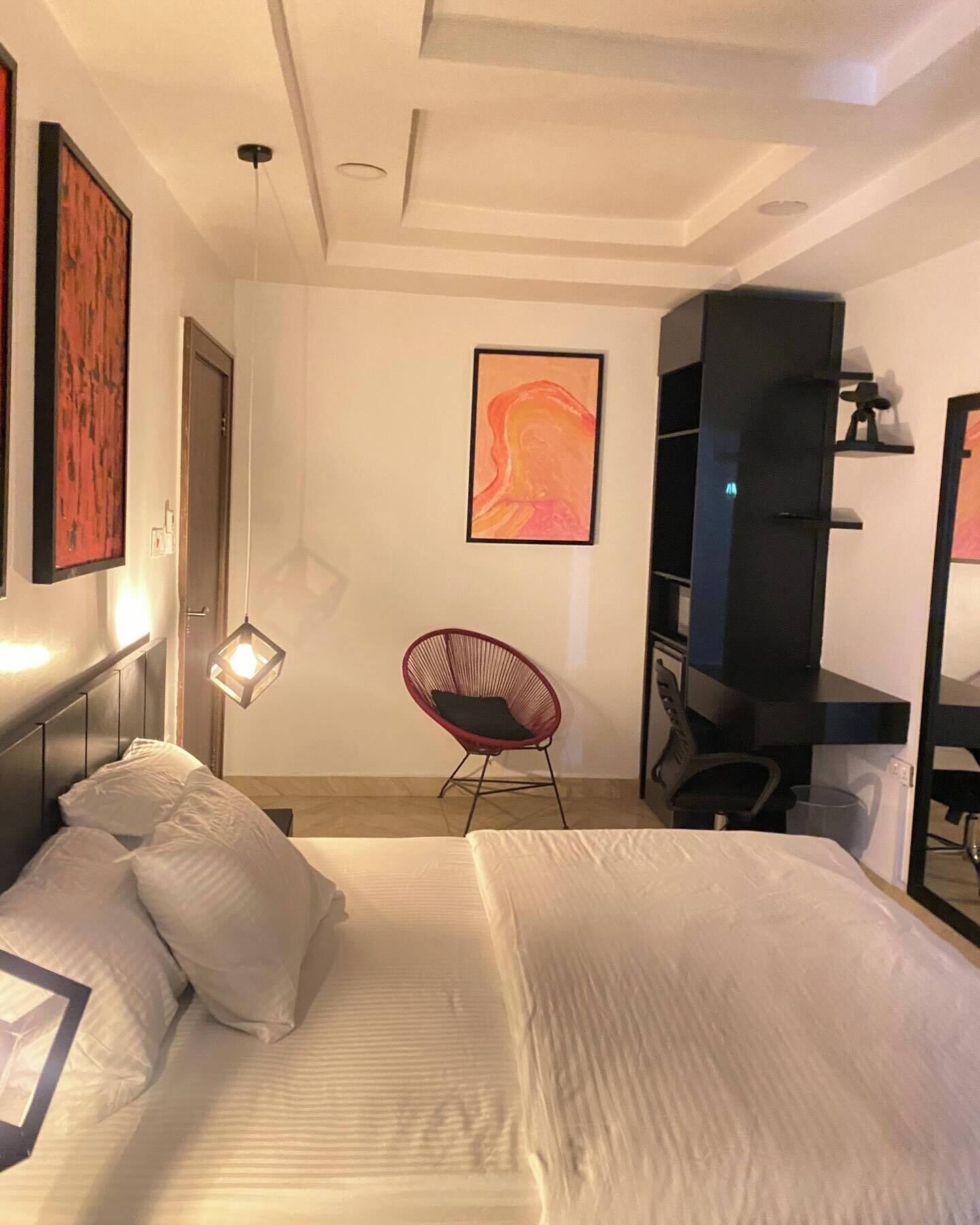 Une chambre d’hôtel moderne avec un grand lit, un fauteuil rouge, un bureau et des œuvres d’art accrochées aux murs.