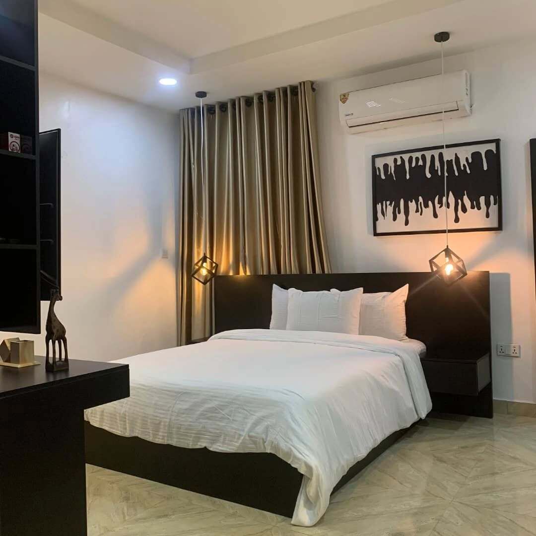 A modern bedroom with a bed, a nightstand, a wall-mounted air conditioner, and a painting.