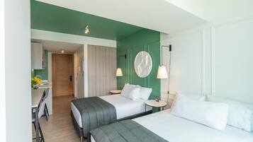 Quarto de hotel moderno com duas camas, uma escrivaninha e uma parede verde de destaque.