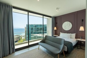 Una habitación de hotel moderna con un ventanal grande, una cama, un sofá y un reloj de pared redondo.