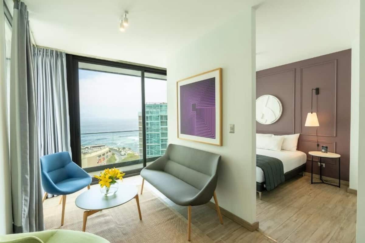 A hotel room with a bed, a desk, a chair, and a large window with a view of the city.