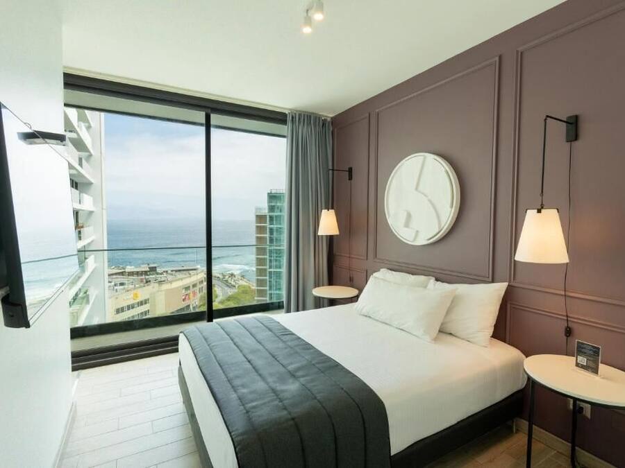 A modern hotel room with a large bed, a view of the city, and a balcony.