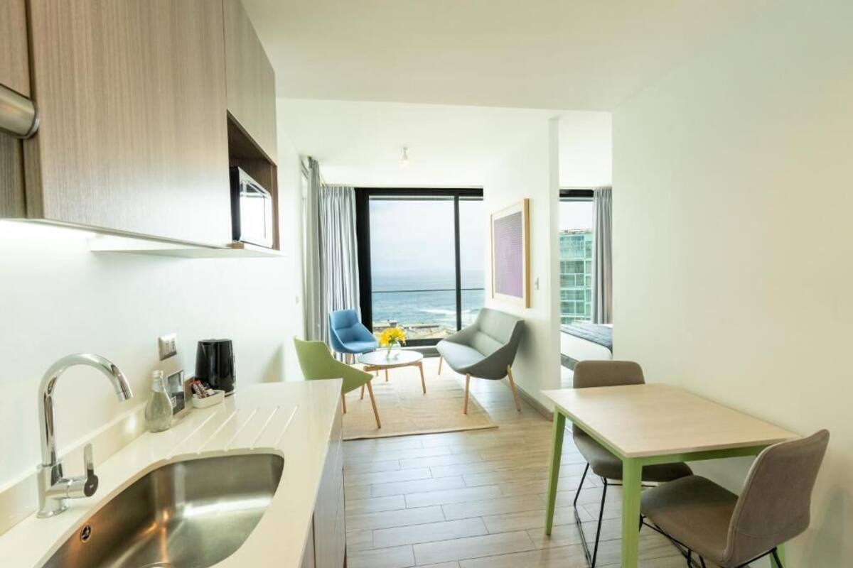 A modern kitchen with a sink, a dining area with a table and chairs, and a view of the ocean through large windows.