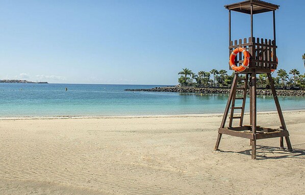 Une tour de surveillance sur une plage, avec une eau d’un bleu limpide et des palmiers en arrière-plan.