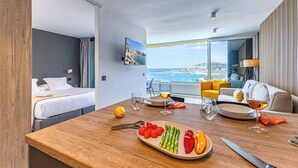 Habitación de hotel con zona de comedor, cama y vista al mar.