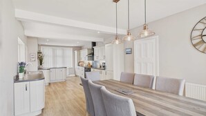 Une cuisine moderne avec des meubles blancs, une table à manger en bois et des chaises recouvertes d’un tissu gris.