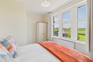 A bedroom with a bed, a wardrobe, and a window with a view of a green field and a house. - Host Stay Chirnells (Bamburgh)