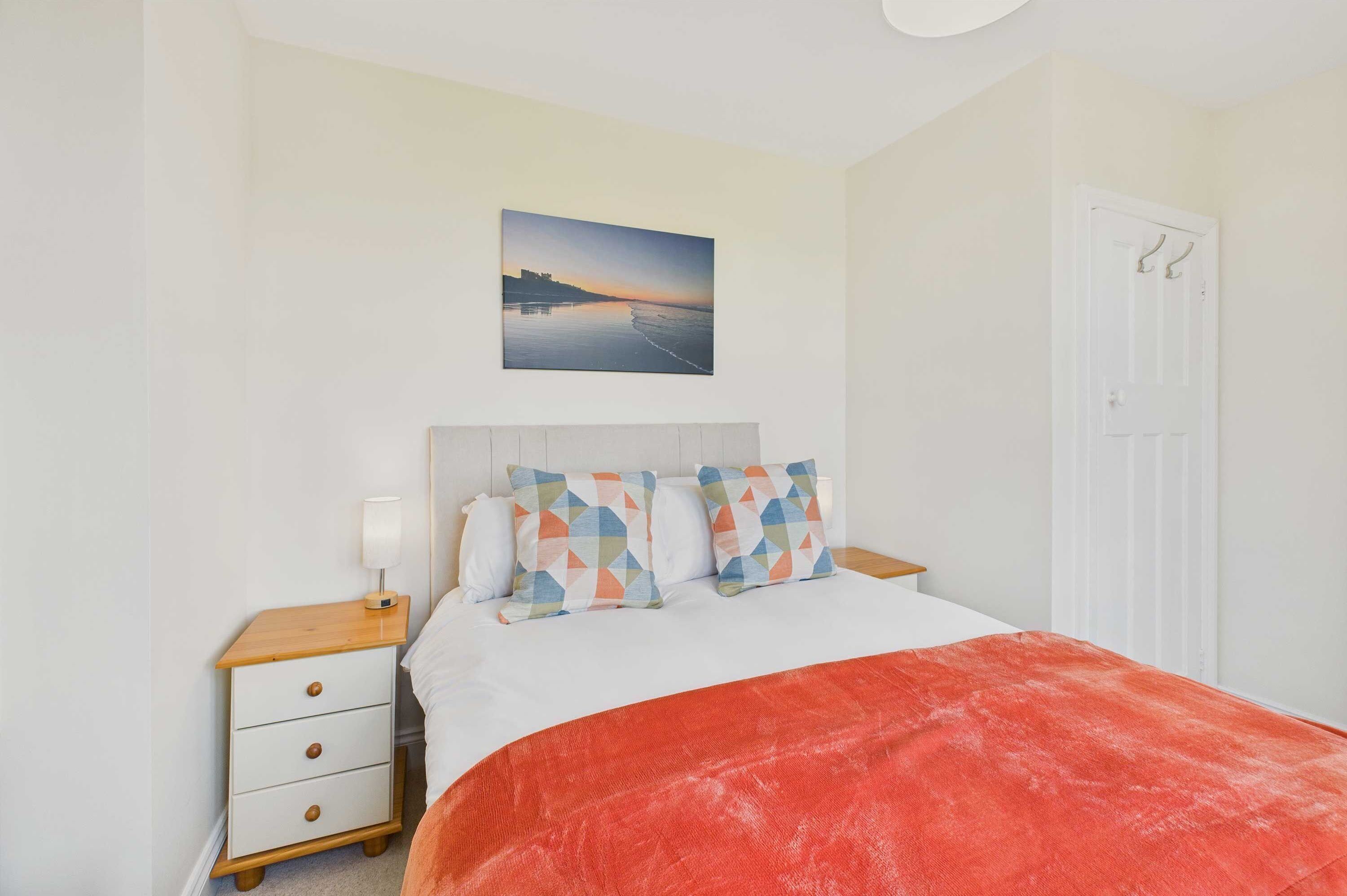 Une chambre à coucher avec un lit, une table de chevet, un tableau et une porte.