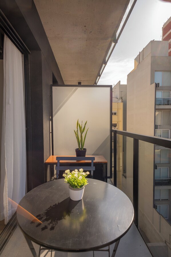 Enjoy a tranquil balcony retreat with a round table, potted plant, and glass railing offering a view of the surrounding buildings.