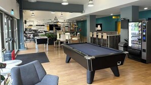 Une table de billard dans un espace intérieur moderne, avec des sièges et un distributeur automatique.