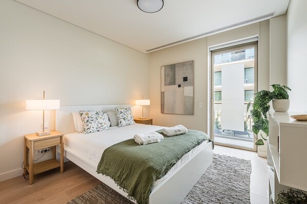 Un dormitorio moderno con una cama, dos mesitas de noche con lámparas, una manta verde, un ventanal grande y una planta en maceta.