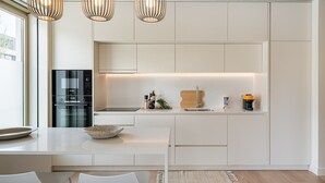 Una cocina moderna con armarios blancos, horno empotrado y comedor con mesa y sillas blancas.