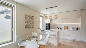 Una cocina moderna con una mesa de comedor de vidrio, sillas blancas e iluminación colgante.