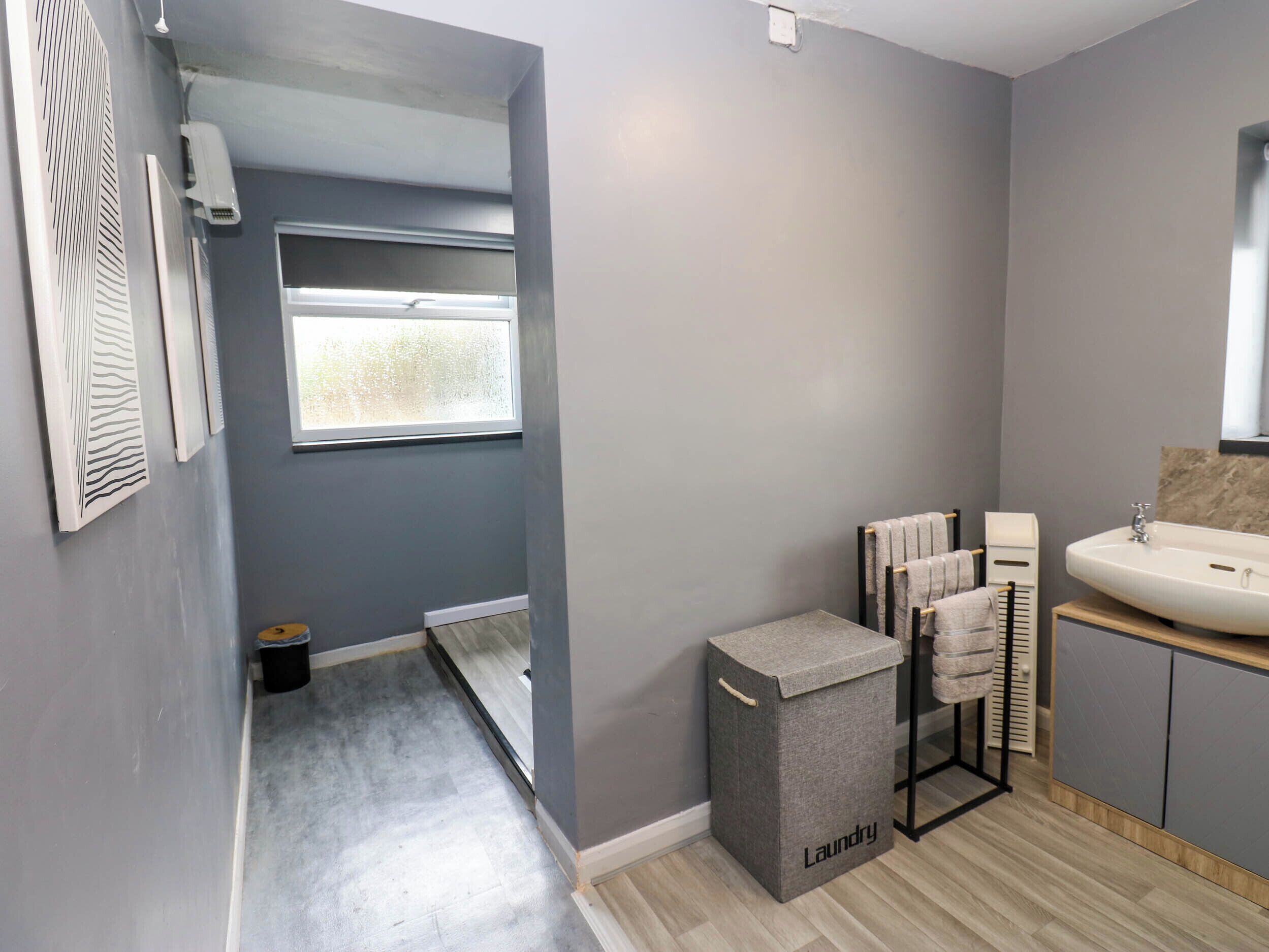 A modern bathroom with a grey wall, a window, a sink, and a laundry basket.
