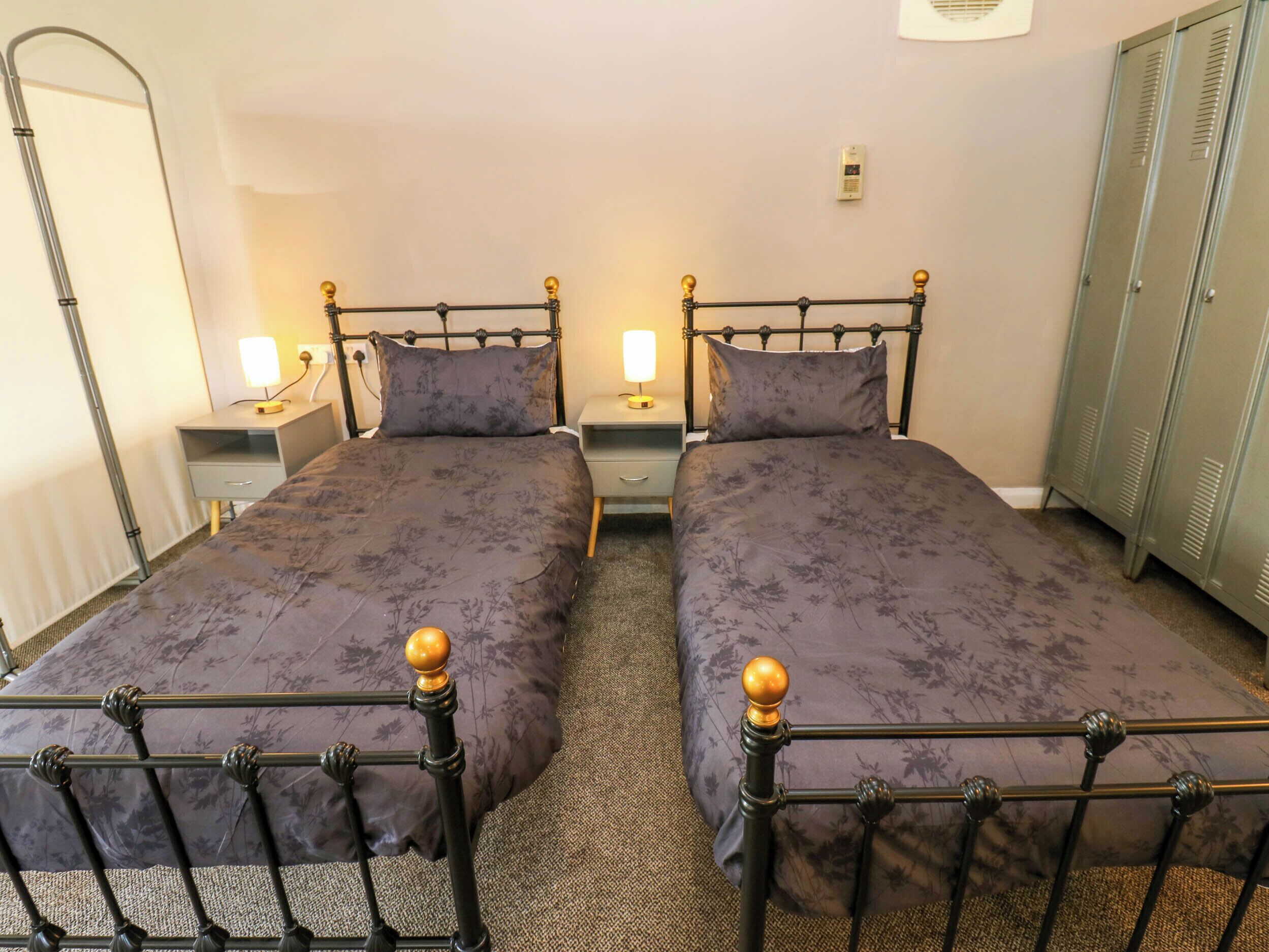 A twin room with two single beds, nightstands with lamps, a radiator, and a wardrobe.