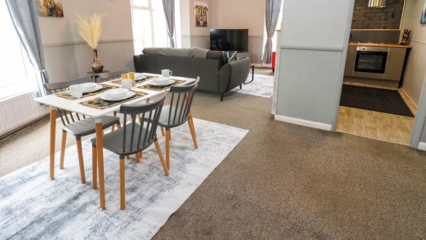 Una sala de estar moderna con comedor, sofá gris, televisor de pantalla plana y cocina equipada con horno.
