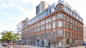 A multi-story building with a mix of brick and modern glass facades, featuring a prominent corner turret and a cylindrical structure on the roof. - Student Only Swanston House (Belfast)