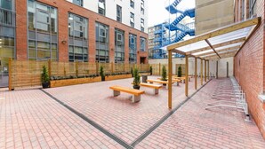 A courtyard with brick flooring, wooden benches, and planters. - Student Only Swanston House (Belfast)