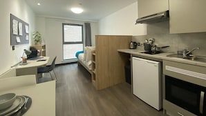 A modern kitchen with a dishwasher, stove, and sink. There is a dining table with plates and cutlery. A window with a view of the outside is visible. - Student Only Swanston House (Belfast)