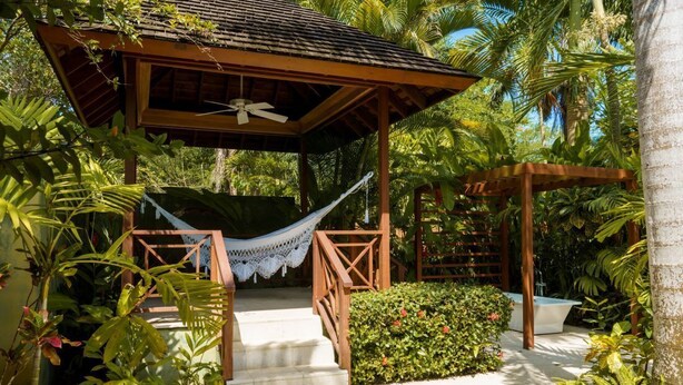 Un belvédère en bois doté d’un ventilateur de plafond, entouré d’une végétation tropicale luxuriante et agrémenté d’un hamac.