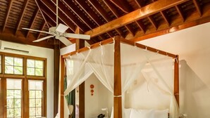 Un lit à baldaquin avec quatre poteaux, un ventilateur de plafond et une table de chevet avec une lampe.