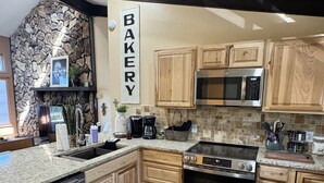A kitchen with wooden cabinets, a stone accent wall, a built-in oven, and a microwave. - Newly Renovated 5 bedroom Condo in Ruidoso (Ruidoso)