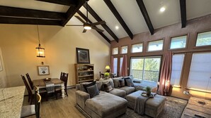 A spacious living room with a large sectional sofa, a dining table with chairs, and a fireplace. There are large windows with curtains, a ceiling fan, and a hanging light fixture. - Newly Renovated 5 bedroom Condo in Ruidoso (Ruidoso)