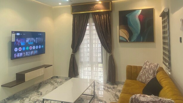Een moderne woonkamer met een flatscreen televisie, een bank, een salontafel en een groot raam met gordijnen.